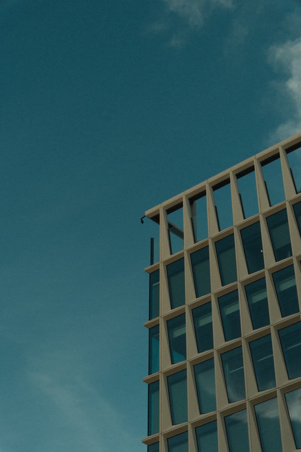 The upper stories of a glass-and-concrete building rising into a broad blue sky, with a small cloud at the edge.